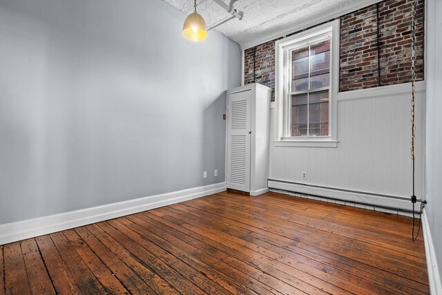 empty room featuring hardwood / wood-style floors, a baseboard radiator, and brick wall