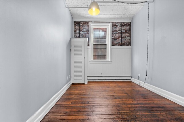 unfurnished room featuring brick wall, dark hardwood / wood-style floors, and a baseboard heating unit