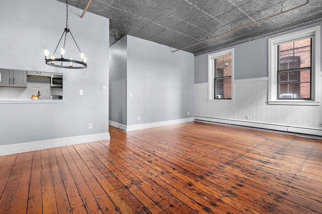 empty room with an inviting chandelier, hardwood / wood-style flooring, and a baseboard radiator