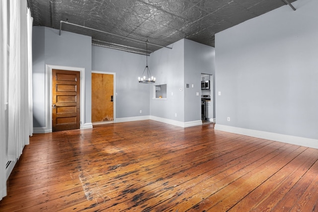 unfurnished living room featuring hardwood / wood-style floors, a high ceiling, and an inviting chandelier