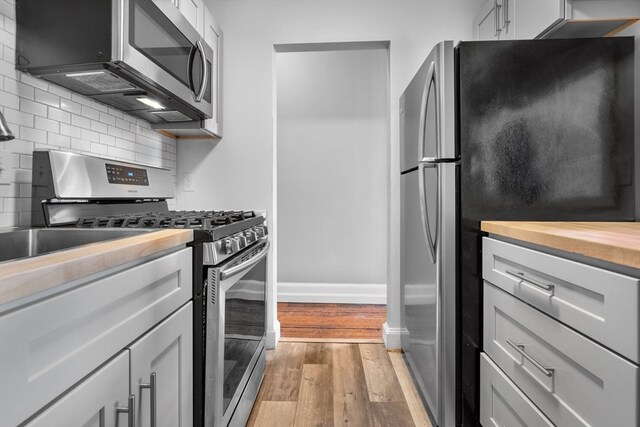 kitchen featuring light hardwood / wood-style floors, backsplash, appliances with stainless steel finishes, and wooden counters