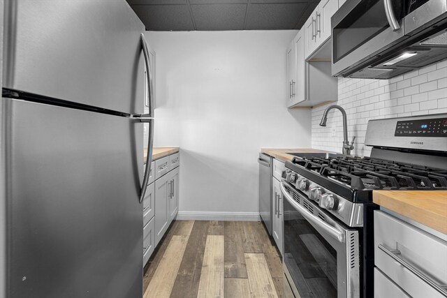 kitchen featuring stainless steel appliances, white cabinetry, hardwood / wood-style floors, wood counters, and decorative backsplash