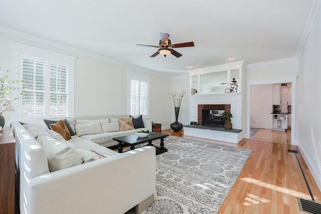 living room with ceiling fan, ornamental molding, a brick fireplace, and light hardwood / wood-style flooring