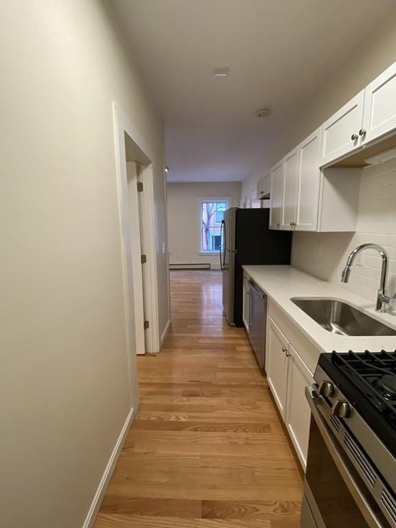 kitchen featuring sink, decorative backsplash, light wood-type flooring, white cabinetry, and stainless steel appliances