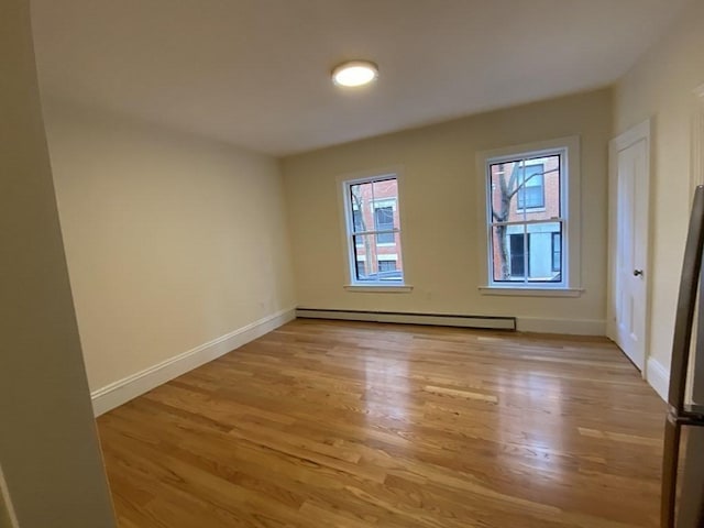 empty room with light wood-type flooring and a baseboard heating unit