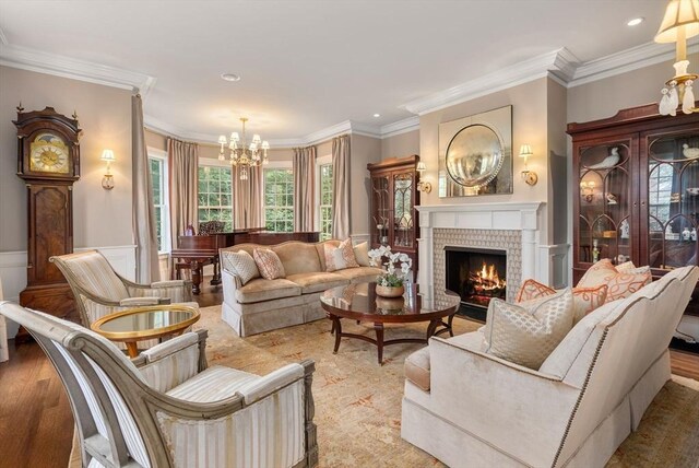 living room with hardwood / wood-style flooring, ornamental molding, a brick fireplace, and a notable chandelier