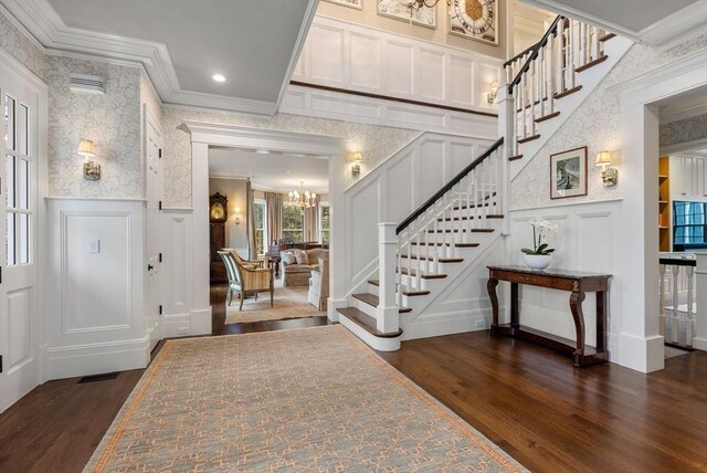 entrance foyer featuring an inviting chandelier, dark wood-type flooring, and ornamental molding