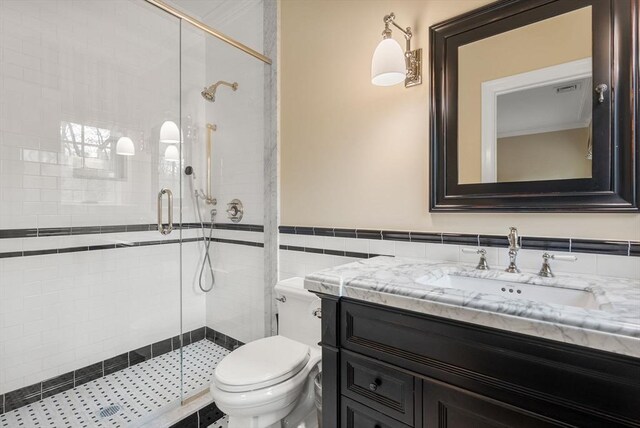 bathroom with vanity, toilet, a shower with shower door, and tile walls