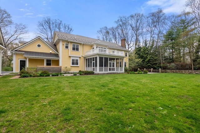 rear view of house with a lawn, a sunroom, and a balcony