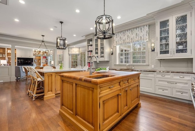 kitchen with pendant lighting, a wealth of natural light, white cabinetry, sink, and a center island with sink