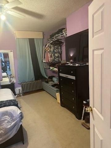 carpeted bedroom featuring ceiling fan, radiator heating unit, and a textured ceiling