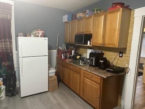 kitchen with light stone countertops, sink, light wood-type flooring, and white refrigerator