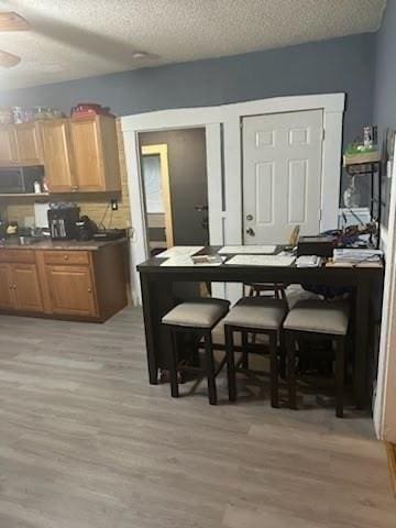 kitchen with ceiling fan, a kitchen bar, light wood-type flooring, and a textured ceiling