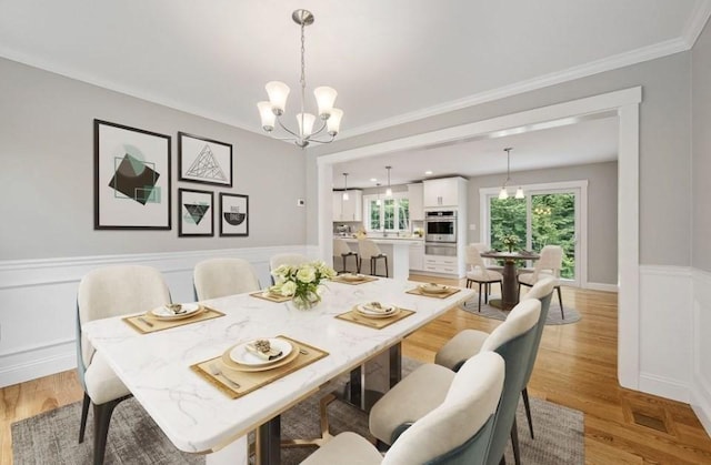 dining area with ornamental molding, a notable chandelier, and light hardwood / wood-style flooring