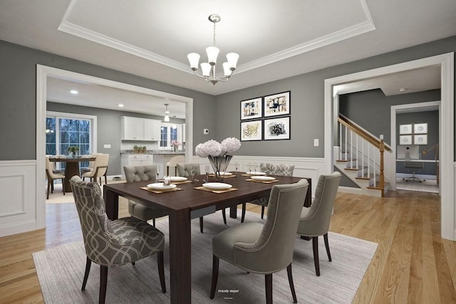 dining room with an inviting chandelier, a tray ceiling, crown molding, and light hardwood / wood-style floors