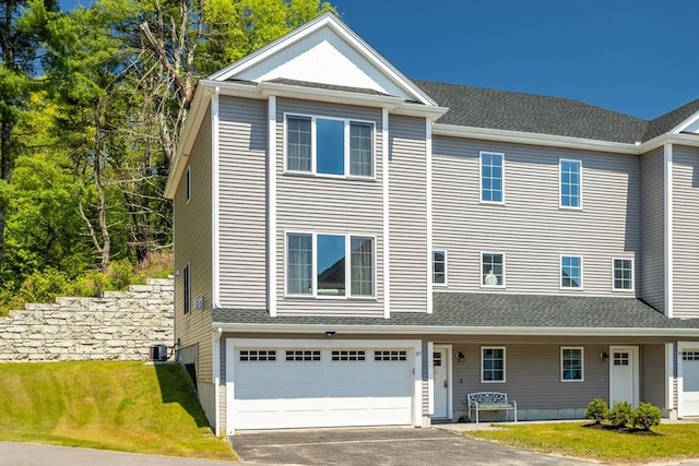 view of property featuring an attached garage, driveway, a front lawn, and central AC unit