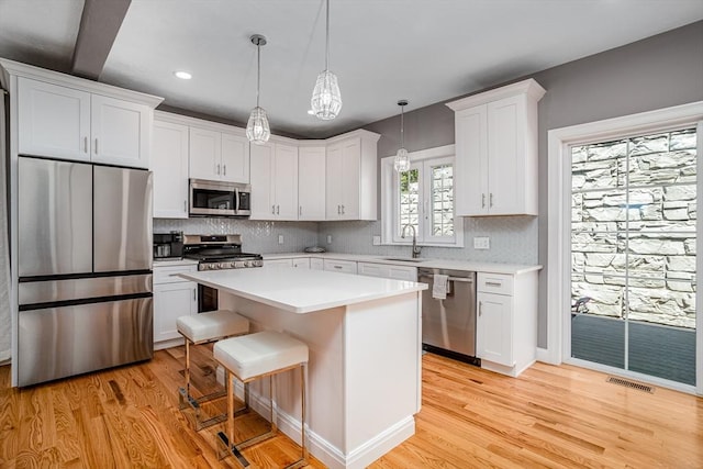 kitchen featuring stainless steel appliances, a sink, light wood-style floors, white cabinets, and tasteful backsplash