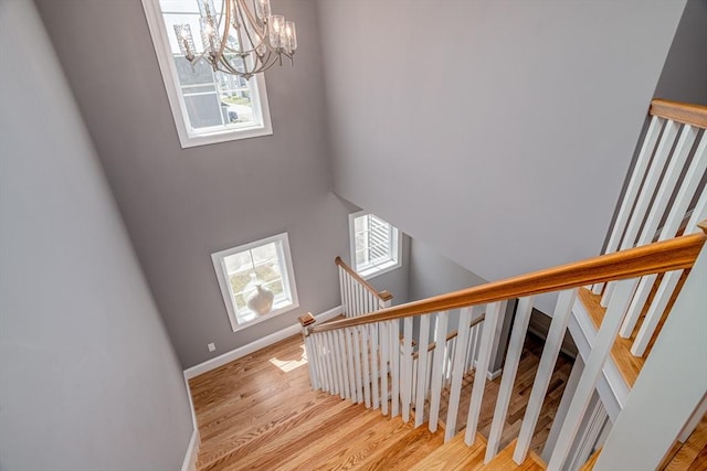 stairs with plenty of natural light, a chandelier, wood finished floors, and baseboards