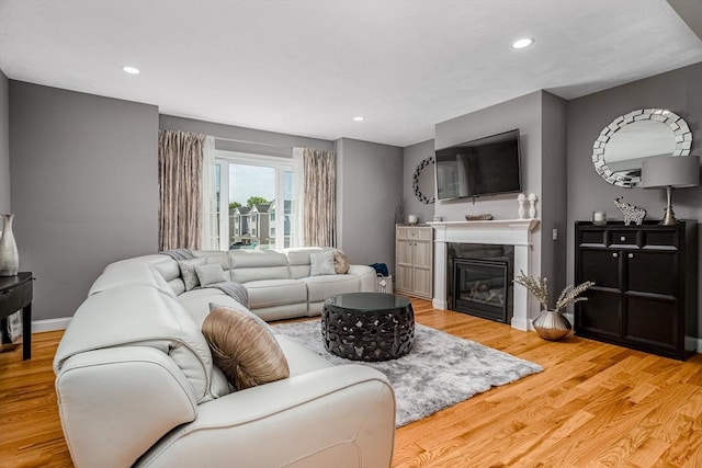 living area featuring light wood-style floors, a glass covered fireplace, recessed lighting, and baseboards