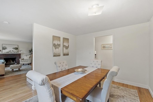 dining area with light wood finished floors, baseboards, and a brick fireplace
