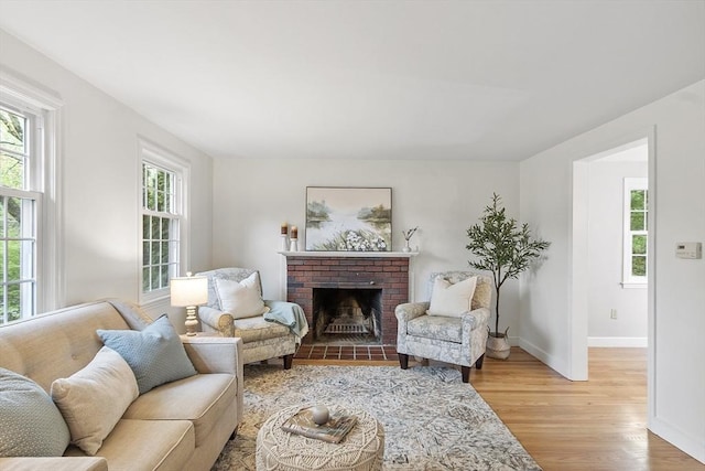 living area featuring light wood-type flooring, baseboards, and a brick fireplace