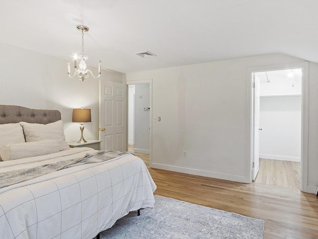 bedroom with light wood finished floors, a chandelier, baseboards, a walk in closet, and vaulted ceiling