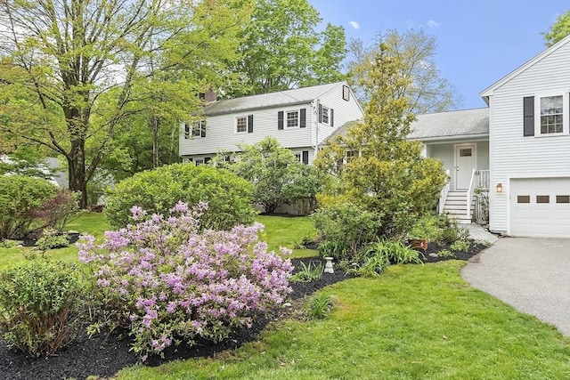 view of front facade with a chimney, a front lawn, a garage, and driveway