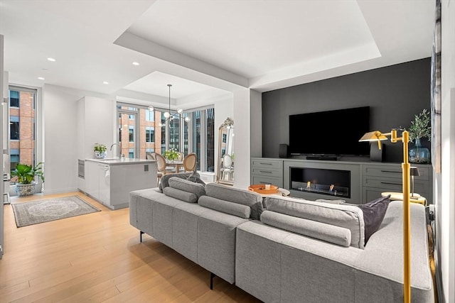 living room with light wood finished floors, a tray ceiling, a fireplace, and recessed lighting