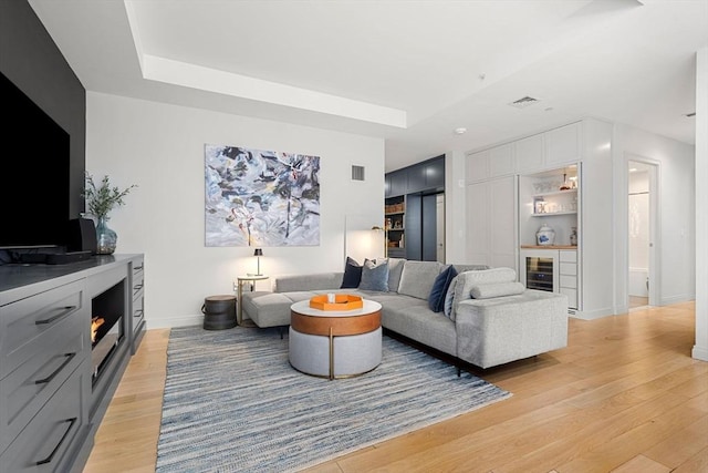 living room featuring light wood-type flooring, baseboards, visible vents, and a raised ceiling