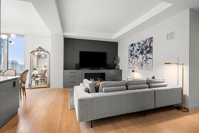 living area with visible vents, baseboards, light wood-style flooring, a view of city, and a tray ceiling