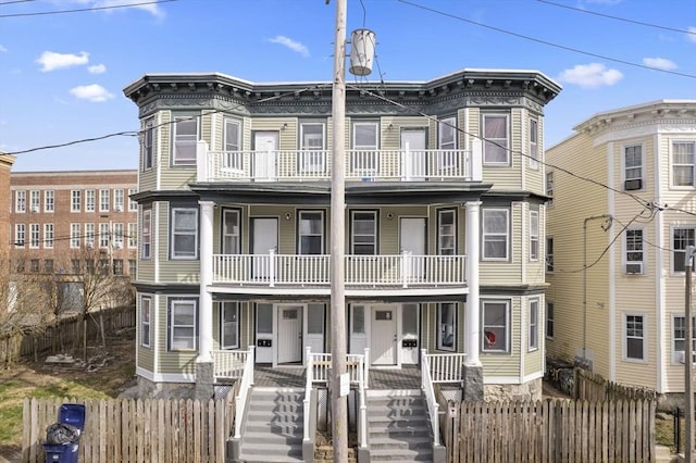 view of property featuring a porch, a balcony, a fenced front yard, and stairs