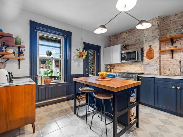 kitchen featuring appliances with stainless steel finishes, a sink, open shelves, wooden counters, and blue cabinetry