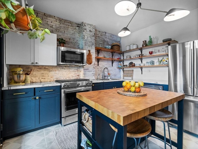 kitchen featuring stainless steel appliances, blue cabinets, a sink, wooden counters, and open shelves
