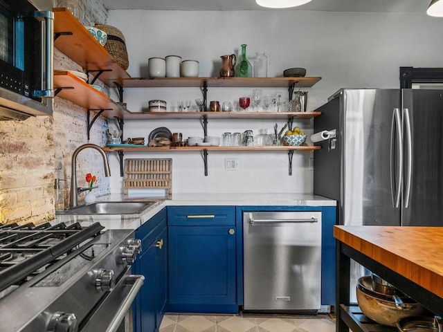 kitchen with blue cabinets, appliances with stainless steel finishes, a sink, open shelves, and decorative backsplash