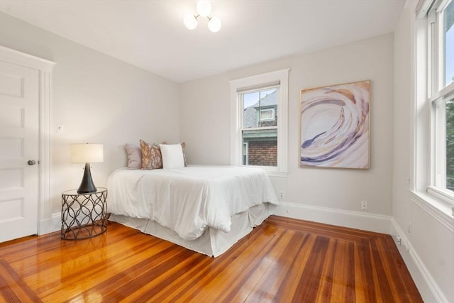 bedroom with multiple windows, wood finished floors, and baseboards