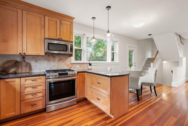 kitchen with stainless steel appliances, light wood-type flooring, a peninsula, backsplash, and pendant lighting