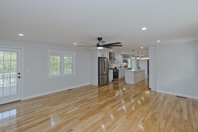 unfurnished living room with light wood-type flooring, recessed lighting, plenty of natural light, baseboards, and ceiling fan
