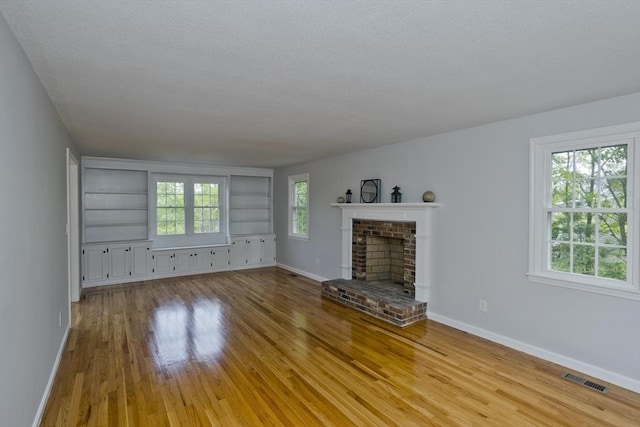 unfurnished living room featuring light wood finished floors, baseboards, healthy amount of natural light, and a textured ceiling