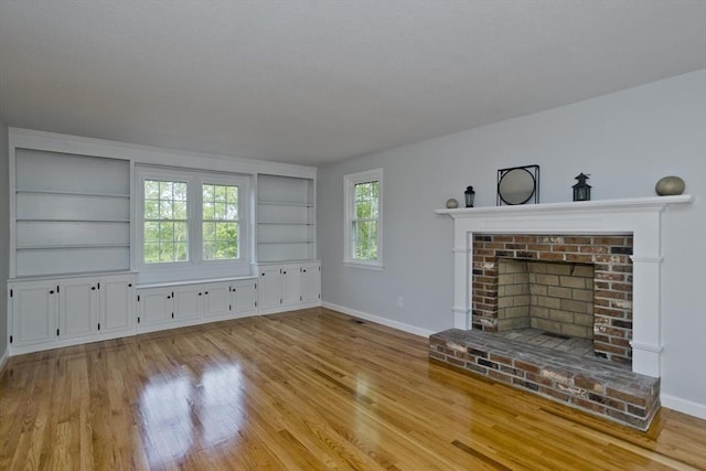 unfurnished living room featuring built in features, baseboards, a fireplace, and wood finished floors