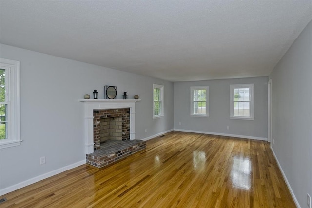 unfurnished living room with light wood finished floors, a brick fireplace, and baseboards