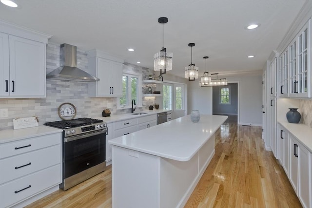 kitchen with appliances with stainless steel finishes, wall chimney range hood, a sink, a kitchen island, and white cabinetry