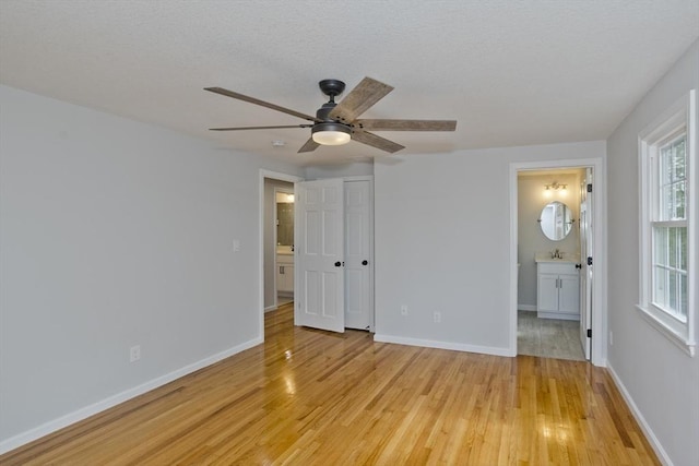 unfurnished bedroom with light wood-style floors, baseboards, and ensuite bath