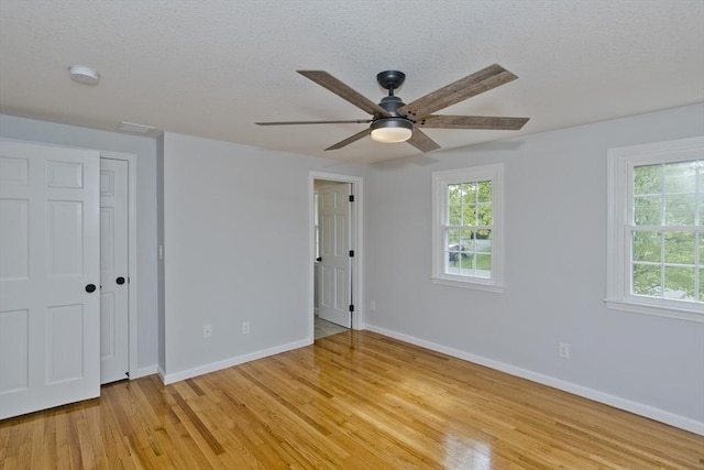 unfurnished bedroom with light wood finished floors, multiple windows, baseboards, a textured ceiling, and a ceiling fan