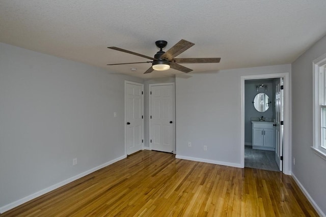 unfurnished bedroom featuring light wood finished floors, baseboards, connected bathroom, a textured ceiling, and a sink