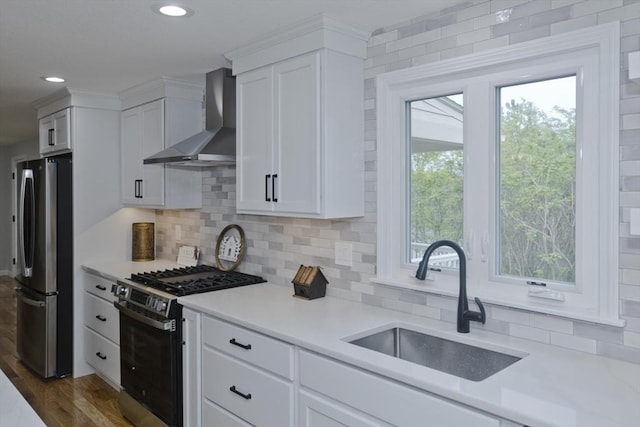 kitchen featuring appliances with stainless steel finishes, wall chimney range hood, a sink, light countertops, and white cabinetry