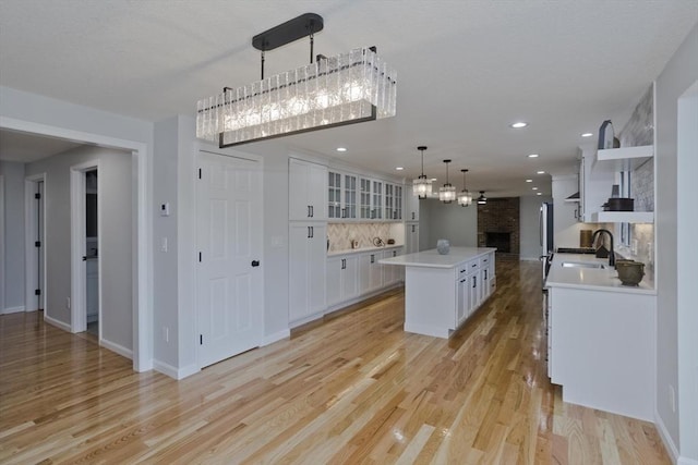 kitchen featuring open shelves, a sink, a brick fireplace, white cabinets, and light countertops