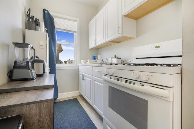 kitchen featuring light countertops, white cabinetry, gas range gas stove, and baseboards