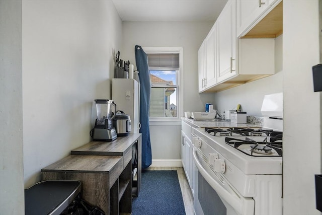 kitchen featuring white range with gas stovetop, a sink, white cabinetry, baseboards, and light countertops