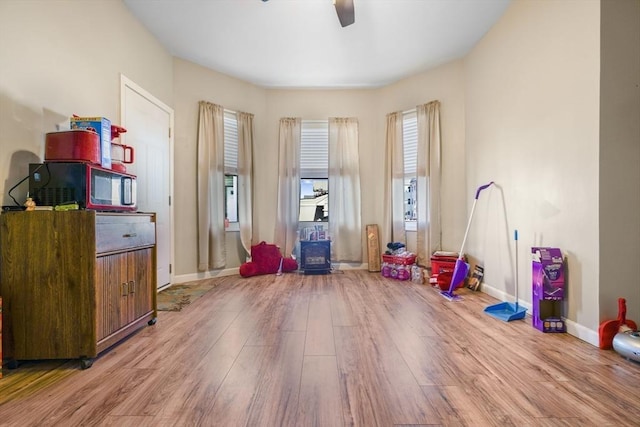 playroom featuring a wood stove, baseboards, ceiling fan, and light wood finished floors