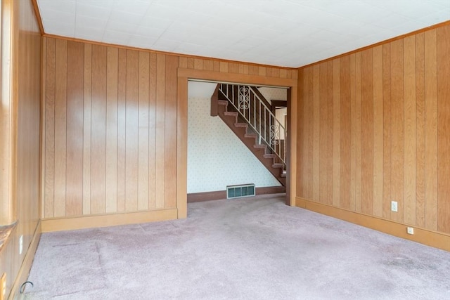 carpeted empty room with stairway, visible vents, and wooden walls